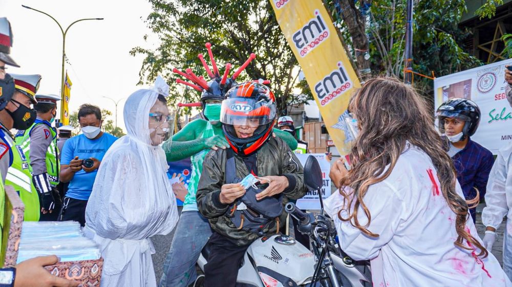 Pocong dan tenaga media membawa himbauan pada pengendara motor dan mobil agar memperhatikan Protokol Kesehatan